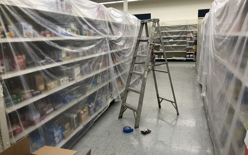 Retail shelves wrapped in plastic after closing with a ladder in the aisle