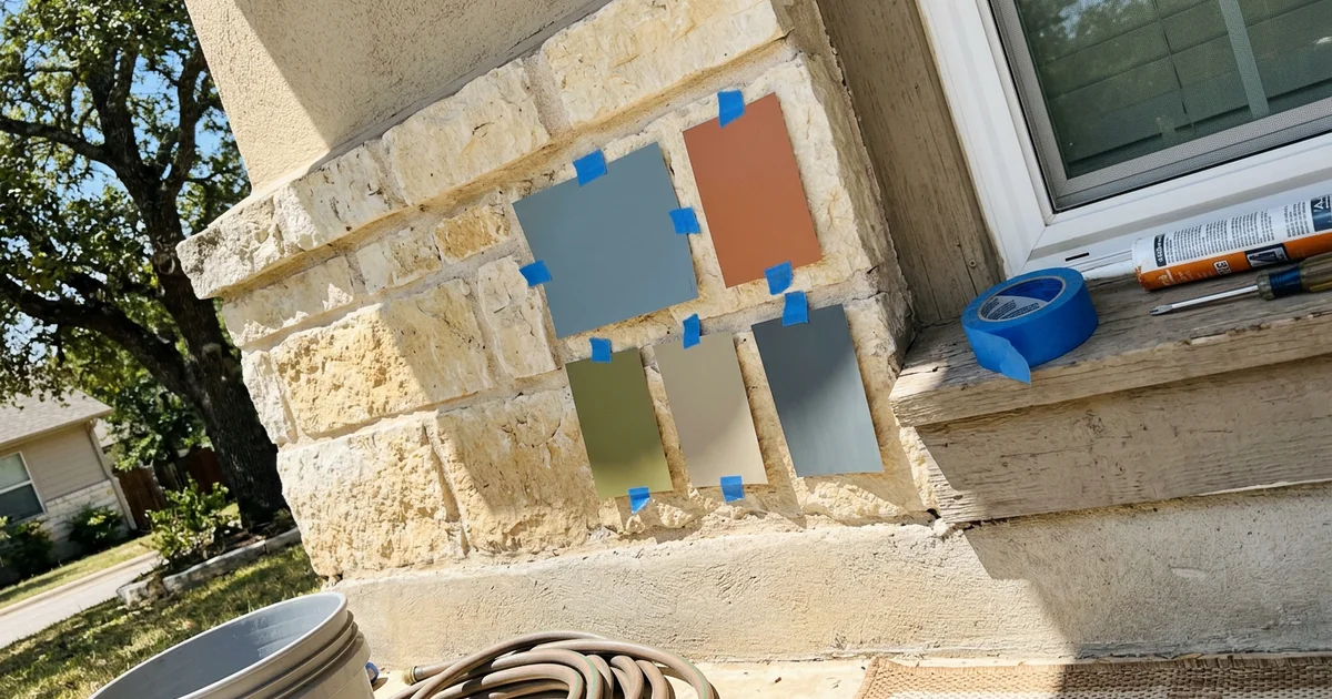 Paint sample swatches taped to a limestone-accented exterior wall in bright afternoon sun