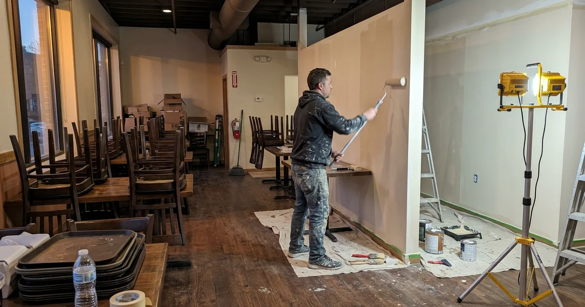 Restaurant dining room after close with chairs stacked on tables and a painter at work