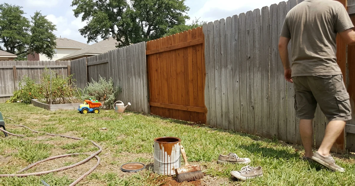 Sun-grayed cedar privacy fence in a Texas backyard with a half-stained section